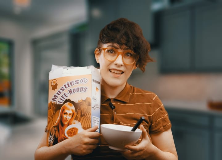 Meljoann holds a bowl of Mustics® Life Hoops cereal. The box features Dr. Synergy Myers on front.